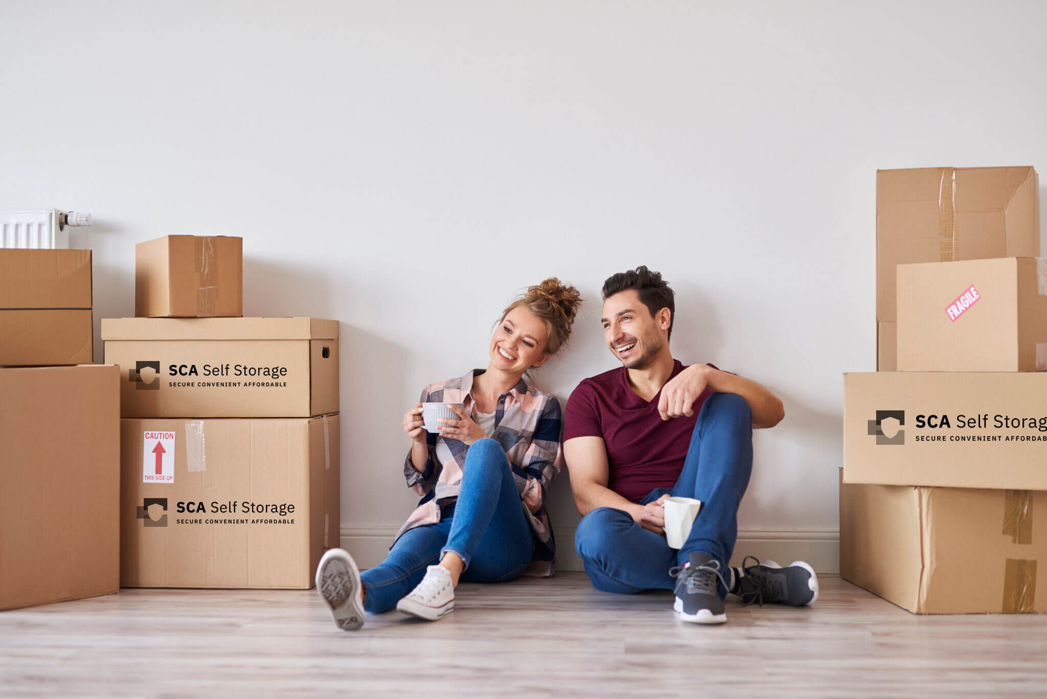 Happy couple with coffee cups relaxing in their new home with SCA Storage Boxes